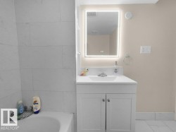 Bathroom vanity featuring a vessel sink, integrated LED mirror, and white cabinetry - 