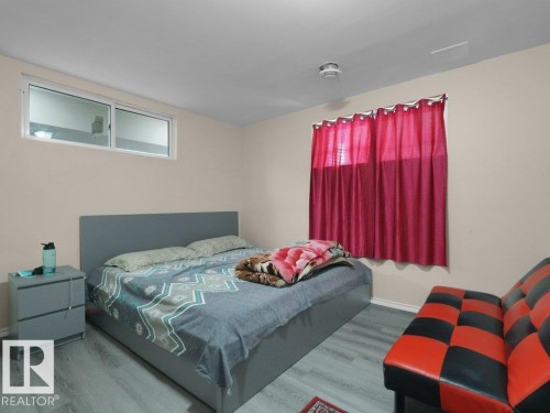Bedroom featuring wood-finish flooring, neutral wall paint, and a window with red drapery - 1419 27 Av, Edmonton, AB 