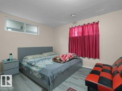 Bedroom featuring wood-finish flooring, neutral wall paint, and a window with red drapery - 