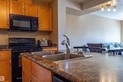 Kitchen featuring a double basin sink with a gooseneck faucet, light wood cabinetry, and a black range with an overhead microwave - 