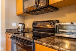 Kitchen featuring a black electric range with an overhead microwave, dark speckled countertops, and light wood cabinetry - 