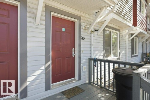 Entry with a rich red paneled door, horizontal siding, and a wooden porch railing - 30 1404 Hermitage Road, Edmonton, AB 