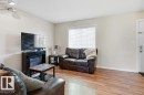 Bright living area featuring wood-finish flooring, light neutral wall paint, white trim, and a window with horizontal blinds - 30 1404 Hermitage Road, Edmonton, AB 