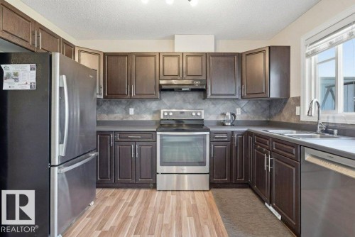 Kitchen featuring dark wood-finish cabinetry, stainless steel appliances, a tiled backsplash, wood-finish flooring, and a large window - 30 1404 Hermitage Road, Edmonton, AB 