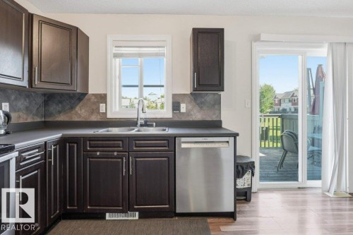 Kitchen featuring dark wood cabinetry, a stainless steel dishwasher, a double basin sink, and a tiled backsplash - 30 1404 Hermitage Road, Edmonton, AB 