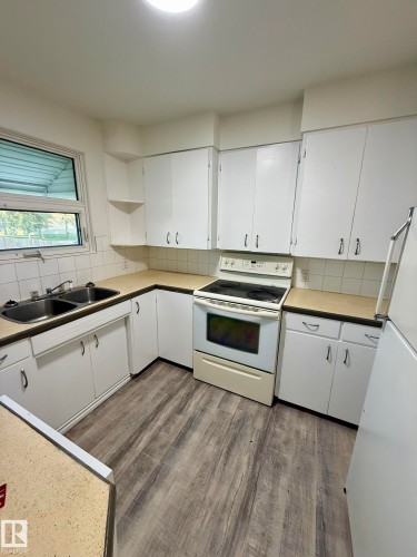Kitchen featuring wood-finish flooring, white cabinetry, a double basin sink, and a white electric range - 10220 107 Street, Westlock, AB - Indoor Photo Showing Kitchen With Double Sink