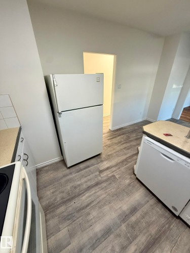 Kitchen area featuring wood-finish flooring, a white refrigerator, and a white dishwasher - 10220 107 Street, Westlock, AB - Indoor Photo Showing Laundry Room