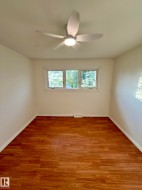 Bright room featuring wood-finish flooring, a contemporary ceiling fan with integrated lighting, and white baseboards - 