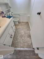 Bathroom featuring a white bathtub with chrome fixtures, a toilet, and a white vanity with paneled doors and black hardware - 