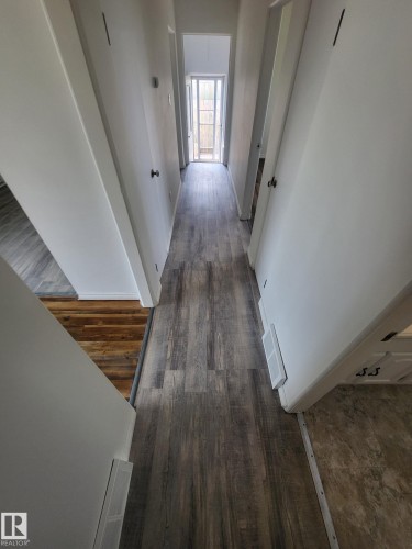 Hallway featuring wood-finish flooring, light-toned walls, and a door with a screen - 10220 107 Street, Westlock, AB - Indoor Photo Showing Other Room