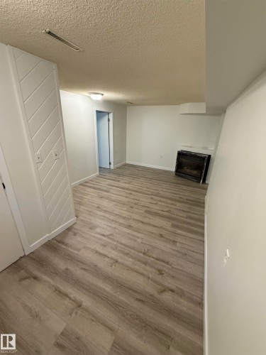 Spacious interior room featuring wood-finish flooring, white painted walls, and a built-in fireplace with a dark surround - 10220 107 Street, Westlock, AB - Indoor Photo Showing Other Room