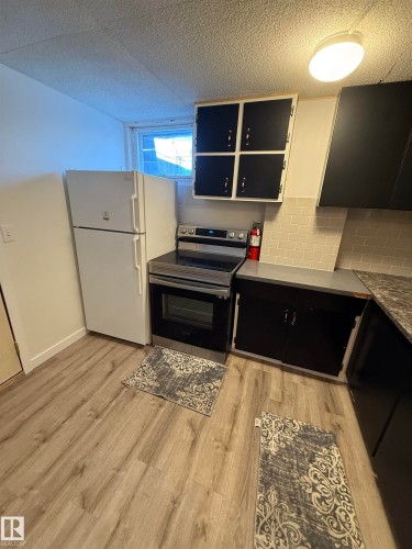 Kitchen area featuring wood-finish flooring, subway tile backsplash, a stainless steel range, and dark cabinetry - 10220 107 Street, Westlock, AB - Indoor