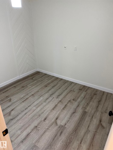 Room featuring wood-finish flooring, white baseboards, and a prominent accent wall with a chevron pattern - 10220 107 Street, Westlock, AB - Indoor Photo Showing Other Room