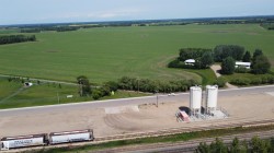 Industrial site featuring two large white storage silos on a concrete pad with surrounding gravel - 