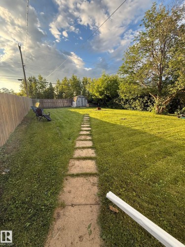 Expansive grassy yard featuring a stepping stone pathway, wood fence, mature perimeter trees, and a utility shed - 10220 107 Street, Westlock, AB - Outdoor With View