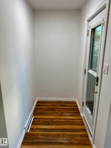 Entryway featuring wood-finish flooring, white baseboards, a white painted wall, and a door with a glass insert - 10220 107 Street, Westlock, AB - Indoor Photo Showing Other Room