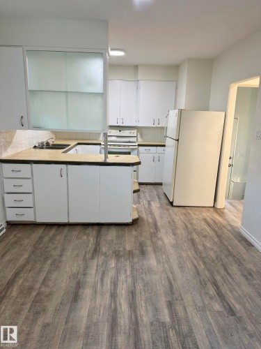 Kitchen featuring wood-finish flooring, white cabinetry, integrated sink, and white appliances - 10220 107 Street, Westlock, AB - Indoor Photo Showing Kitchen With Double Sink