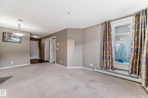 Carpeted living area featuring a large window, neutral paint colors, and a ceiling-mounted light fixture - 121 111 Watt Common, Edmonton, AB 