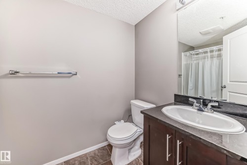 Bathroom featuring a dark wood-finish vanity with a white oval sink, dark countertop, and chrome faucet - 121 111 Watt Common, Edmonton, AB 