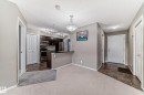 Open-concept living space featuring a kitchen with dark wood-finish cabinetry, stainless steel appliances, and a black countertop with a breakfast bar - 121 111 Watt Common, Edmonton, AB 