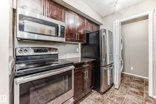 Kitchen featuring stainless steel appliances, dark wood cabinetry, and a stacked washer and dryer unit - 121 111 Watt Common, Edmonton, AB 