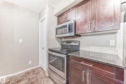 Kitchen featuring dark wood-finish cabinetry, stainless steel range with overhead microwave, dark countertop, and tiled backsplash - 