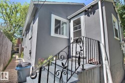 Exterior featuring a stucco finish, multiple windows with white trim, and a side entrance with a black wrought iron railing - 