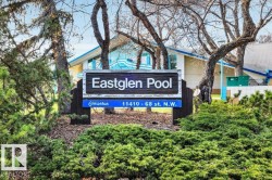 Community sign for Eastglen Pool, featuring a building with blue trim, surrounded by mature trees and manicured shrubbery - 