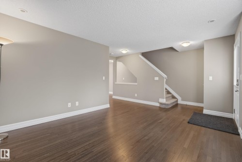 Spacious interior featuring wood-finish flooring, a staircase with carpeted treads, and neutral wall tones - 53 3625 144 Avenue, Edmonton, AB 