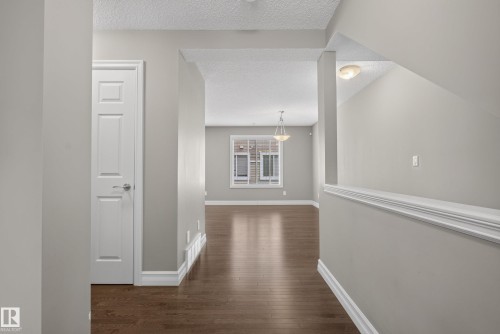 Hallway featuring wood-finish flooring, light grey painted walls, white trim, and a paneled interior door - 53 3625 144 Avenue, Edmonton, AB 