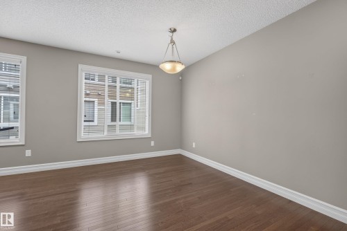 Spacious room featuring rich wood-finish flooring, two large windows with white blinds, neutral wall tones, and crown molding - 53 3625 144 Avenue, Edmonton, AB 