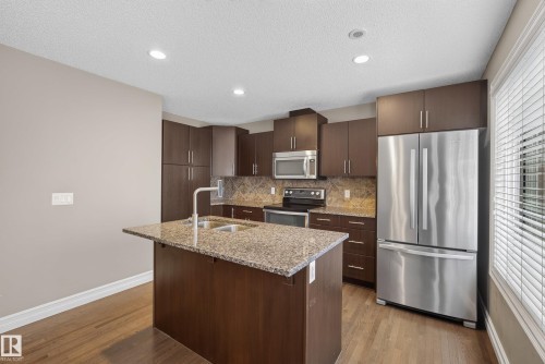 Kitchen featuring an island with a dual-basin sink, granite countertops, wood-finish cabinetry, stainless steel appliances, and recessed lighting - 53 3625 144 Avenue, Edmonton, AB 