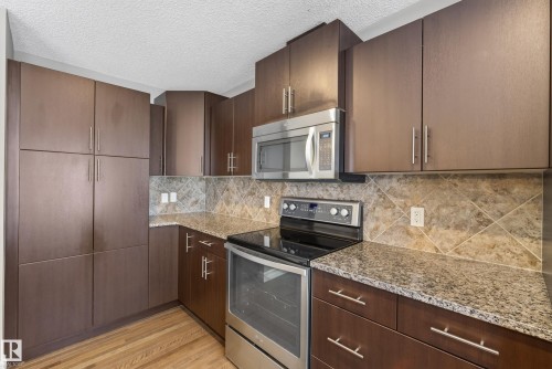 Kitchen featuring wood-finish cabinetry, granite-style countertops, stainless steel appliances, a built-in microwave, and a tiled backsplash - 53 3625 144 Avenue, Edmonton, AB 