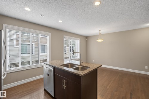 Kitchen island featuring a double basin stainless steel sink, gooseneck faucet, and stone countertop - 53 3625 144 Avenue, Edmonton, AB 