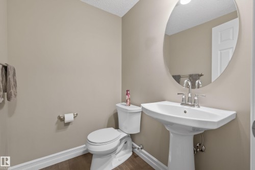 Compact bathroom featuring a white pedestal sink with polished chrome fixtures, a matching toilet, and a large oval mirror - 53 3625 144 Avenue, Edmonton, AB 