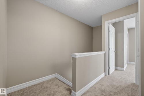 Carpeted hallway with neutral wall paint, white trim, and a partial wall with a cap - 53 3625 144 Avenue, Edmonton, AB 