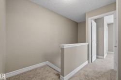 Carpeted hallway with neutral wall paint, white trim, and a partial wall with a cap - 