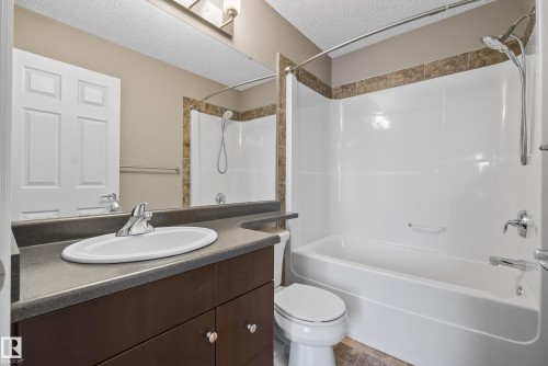 Bathroom featuring a dark wood-finish vanity with an integrated sink, a large mirror, a chrome-finish faucet, a combination shower and bathtub with a white surround, and a coordinating tiled accent border - 53 3625 144 Avenue, Edmonton, AB 