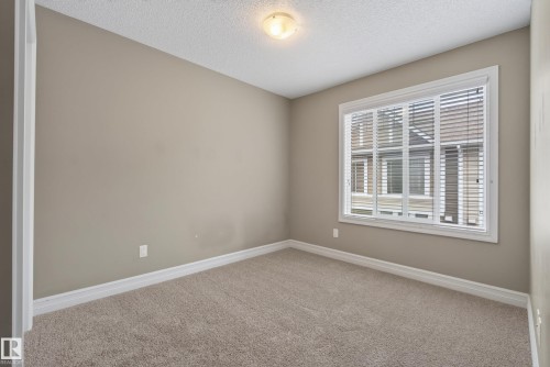 Neutral-toned room featuring a large window with horizontal blinds, textured ceiling, and plush carpeting - 53 3625 144 Avenue, Edmonton, AB 