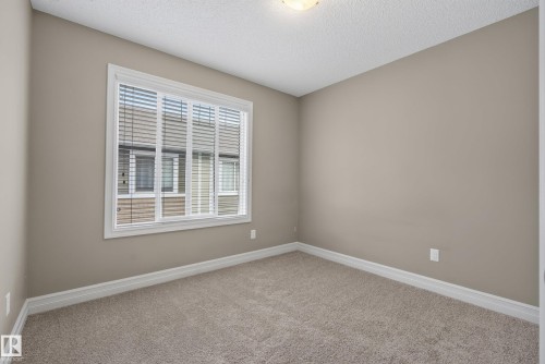Neutral-toned room featuring a large window with white blinds, light beige carpeting, and white baseboards - 53 3625 144 Avenue, Edmonton, AB 