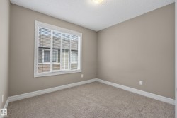 Neutral-toned room featuring a large window with white blinds, light beige carpeting, and white baseboards - 