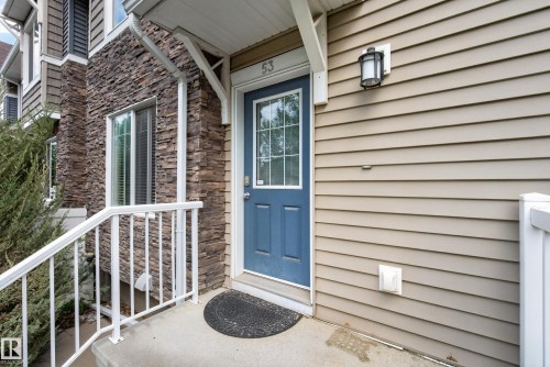 Entryway featuring a blue paneled door with windowpanes, light tan horizontal siding, stacked stone facade, a concrete porch, and white metal railings - 53 3625 144 Avenue, Edmonton, AB 
