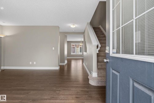 Inviting entryway featuring a paneled front door with decorative glass, wood-finish flooring, a carpeted staircase with white risers, and neutral wall tones - 53 3625 144 Avenue, Edmonton, AB 