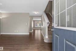 Inviting entryway featuring a paneled front door with decorative glass, wood-finish flooring, a carpeted staircase with white risers, and neutral wall tones - 
