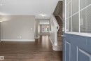 Inviting entryway featuring a paneled front door with decorative glass, wood-finish flooring, a carpeted staircase with white risers, and neutral wall tones - 53 3625 144 Avenue, Edmonton, AB 