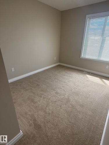 Spacious room featuring neutral carpeting, light-toned wall paint, and white baseboards - 8305 Ellis Crescent Nw, Edmonton, AB 