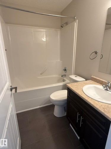Bathroom featuring a white tub and shower combination with a curved shower rod, dark brown vanity with a light-colored countertop, and a white porcelain sink - 8305 Ellis Crescent Nw, Edmonton, AB 