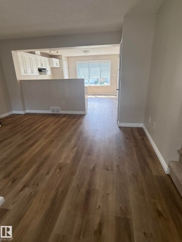 Spacious room featuring wood-finish flooring, white baseboards, and neutral wall tones - 8305 Ellis Crescent Nw, Edmonton, AB 