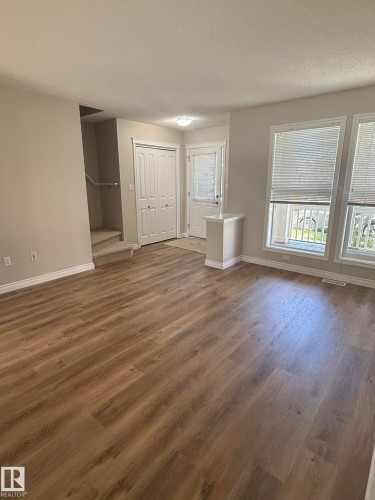 Spacious interior featuring wood-finish flooring throughout, a front entry door with integrated window, and a white bi-fold closet - 8305 Ellis Crescent Nw, Edmonton, AB 