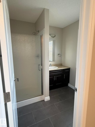 Bathroom featuring a glass-enclosed shower, dark vanity with light countertop, undermount sink, and large format dark tile flooring - 8305 Ellis Crescent Nw, Edmonton, AB 